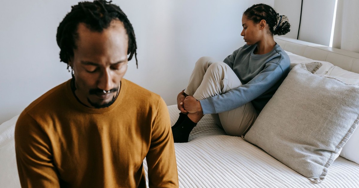 Young black couple in casual outfit spending time on bed with sad face in daytime at home