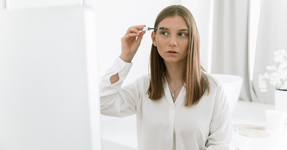 Young woman applying eyebrow makeup in a bright modern indoor bathroom setting.