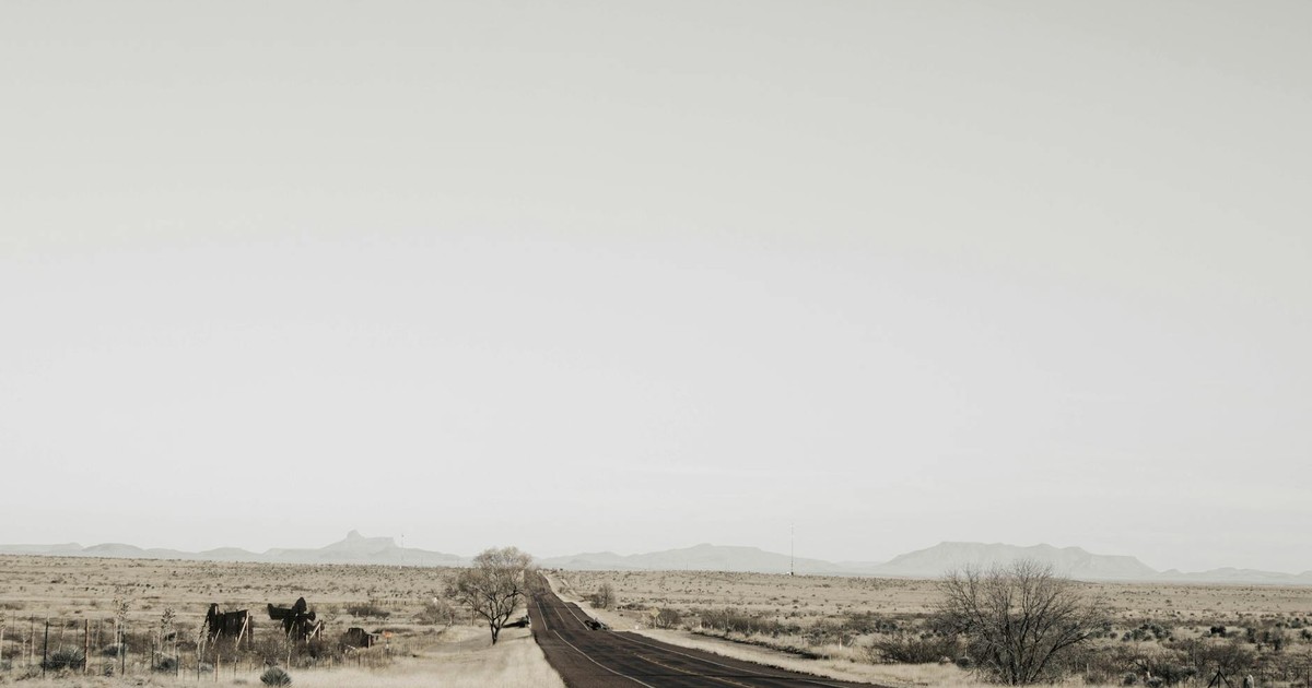 A solitary road cutting through the vast plains of Marfa, Texas, under an expansive sky.