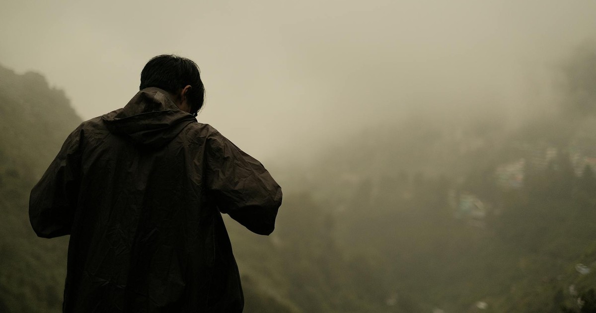 Silhouette of a person in a jacket standing on a foggy mountaintop overlooking a mist-covered valley.