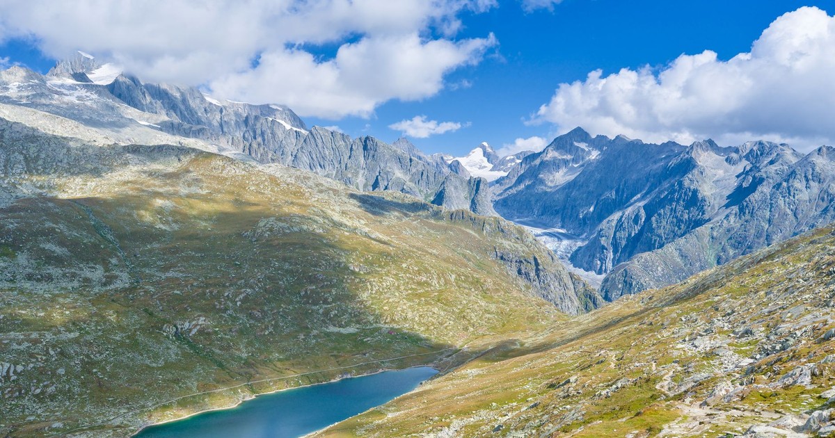 A breathtaking view of the Swiss Alps with a tranquil lake and rugged mountain peaks under a vibrant sky.