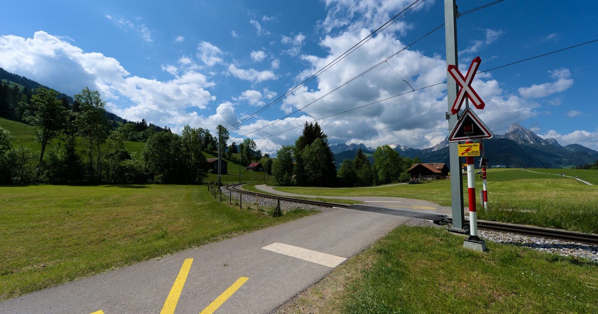 A picturesque railway crossing in Saanen, Switzerland, framed by the Swiss Alps under a bright sky.