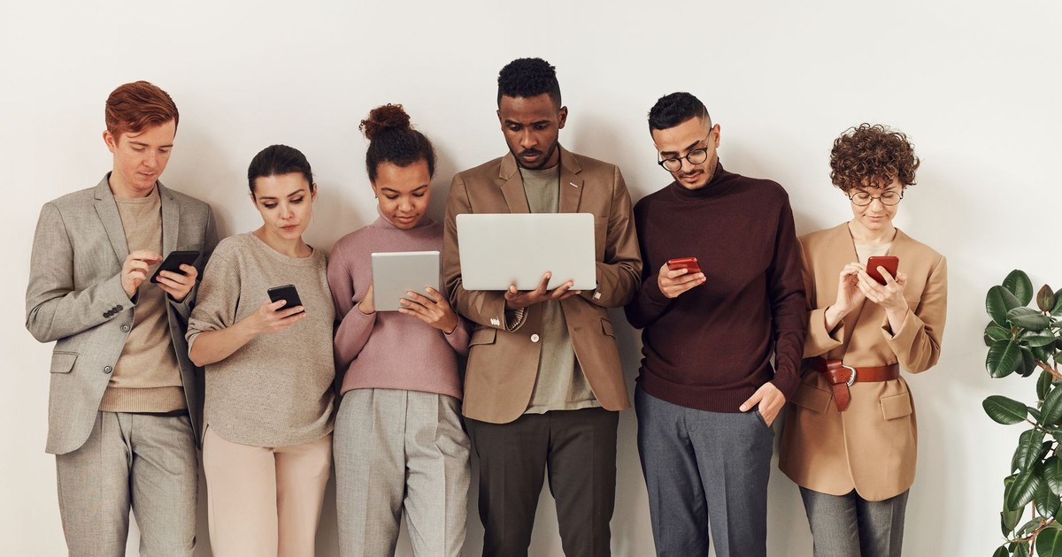 A diverse group of adults interacting with various devices in a stylish office setting, showcasing modern technology use.