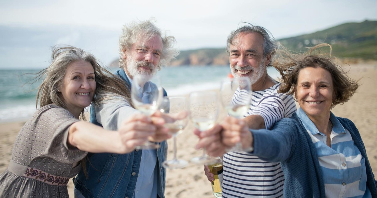 Senior adults enjoying a coastal toast with wine on a Portuguese beach, celebrating friendship.