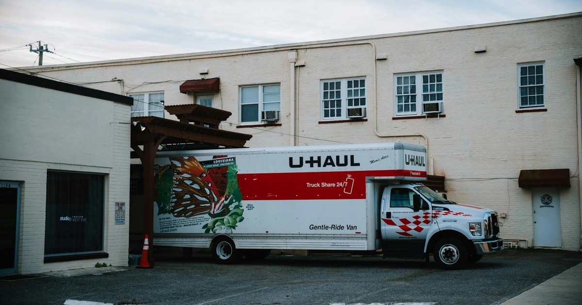 A U-Haul moving truck parked in front of a beige warehouse building.