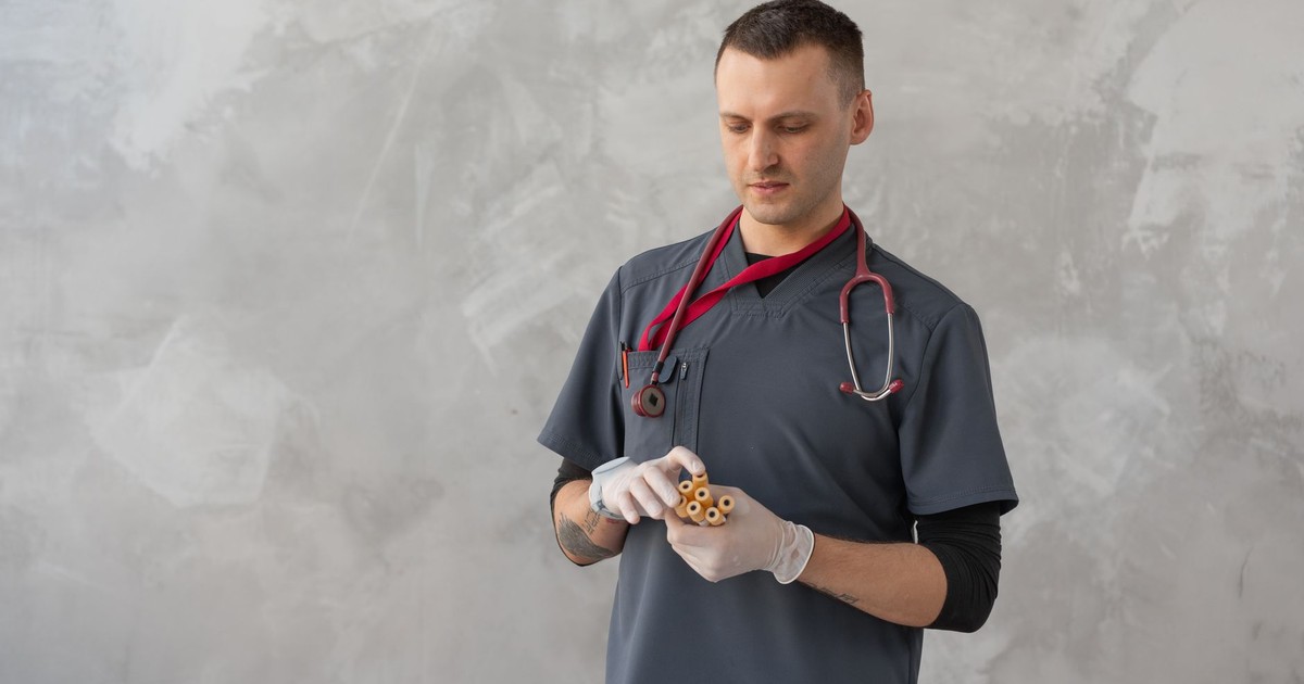 Male healthcare worker in gray scrub suit examining test tubes in a clinical setting.