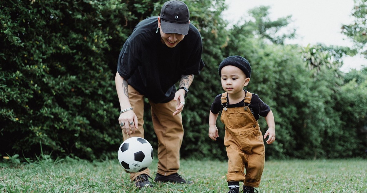 Father and young son enjoying playing soccer together in a lush green park.