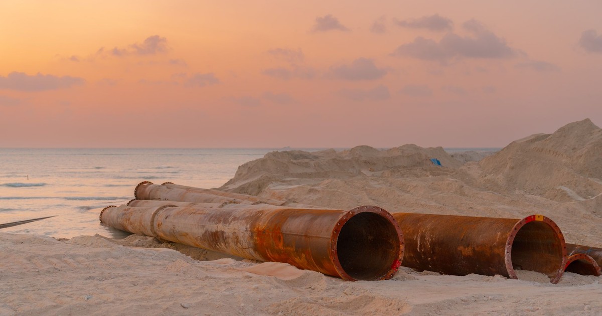 Rusty pipes at a coastal construction site with scenic sunset view.