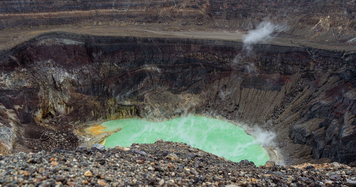 Panoramic view of an active volcano crater with steaming fumaroles and a striking turquoise lake.