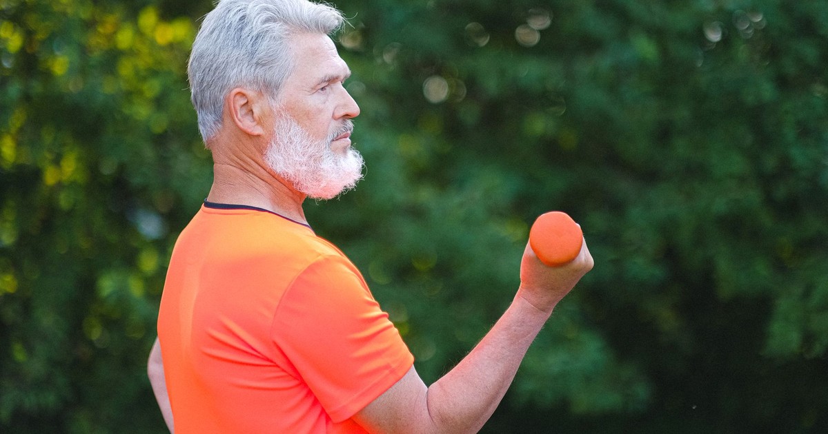 Side view of concentrated senior man in sportswear doing exercise with dumbbells for arms in daytime