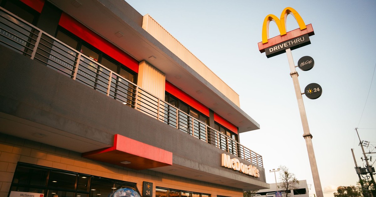 A modern McDonald's fast food restaurant with distinctive branding and drive-thru facilities under a clear blue sky.