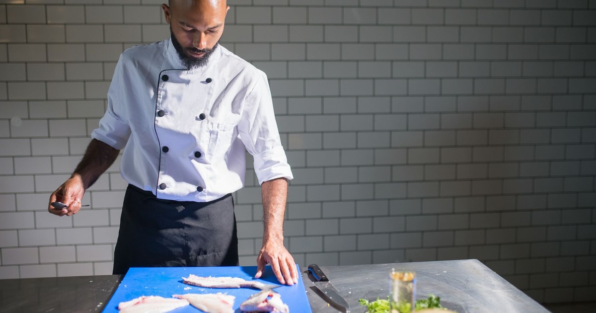 Chef in restaurant kitchen filleting fish on cutting board, focusing on culinary skills.