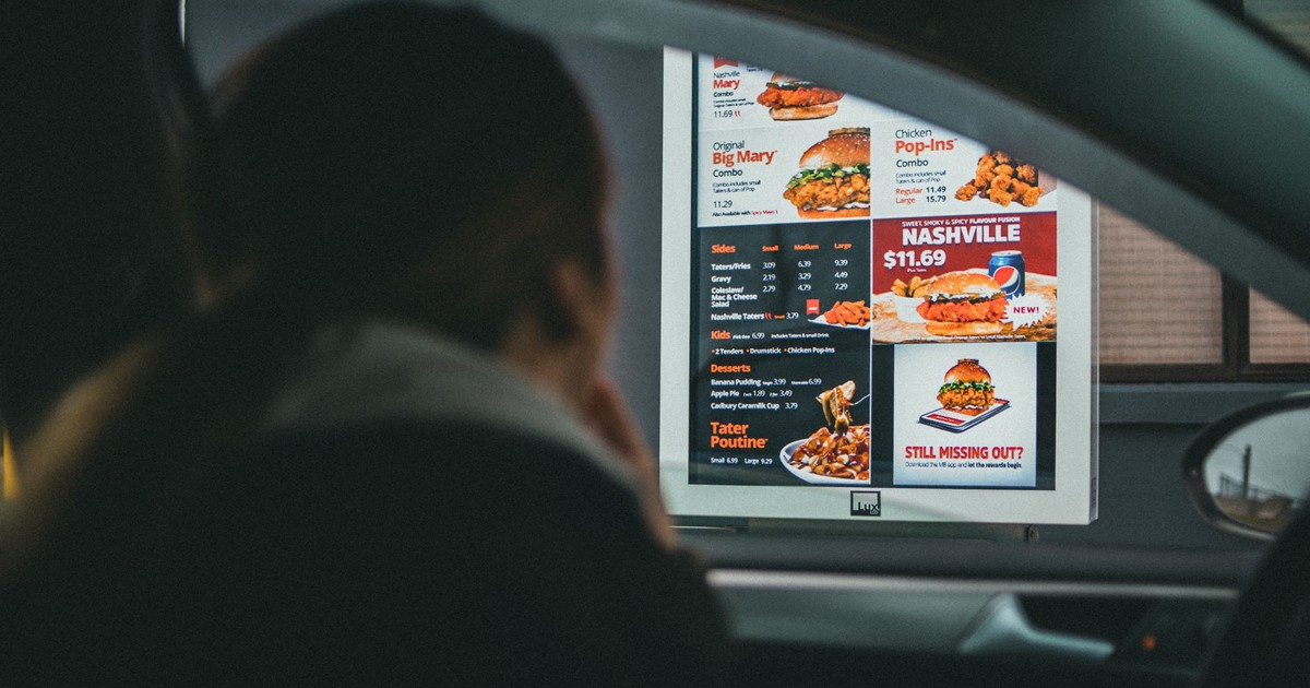 A woman in a car views the menu at a fast food drive-thru, ready to order her meal.