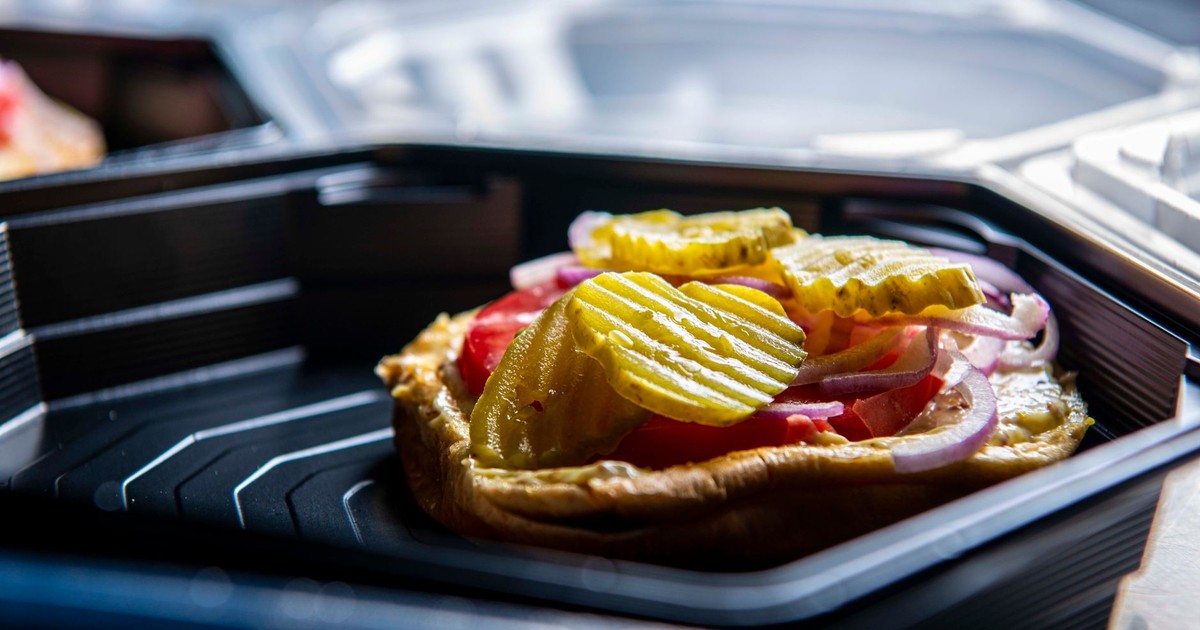 A delicious sandwich with pickles, onions, and tomatoes in a takeout container, showcasing a close-up view.