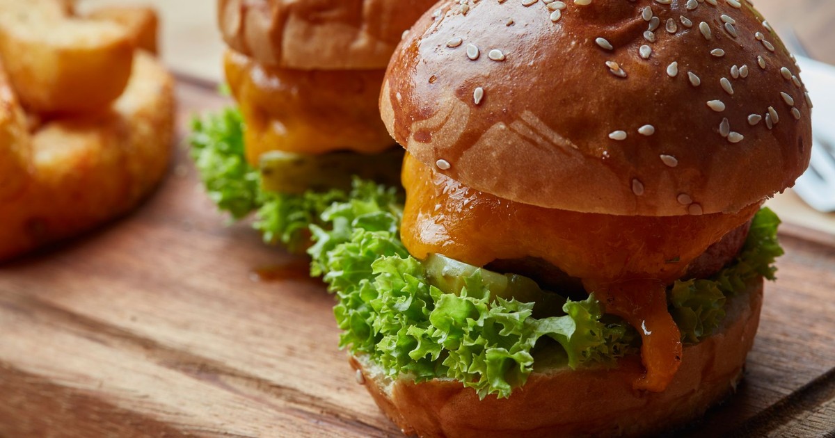 Close-up of juicy cheeseburgers with lettuce and pickles served on a wooden board.