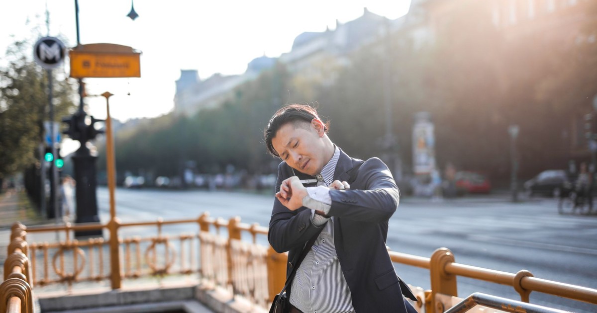Asian businessman in suit checks time while standing outdoors by city metro entrance