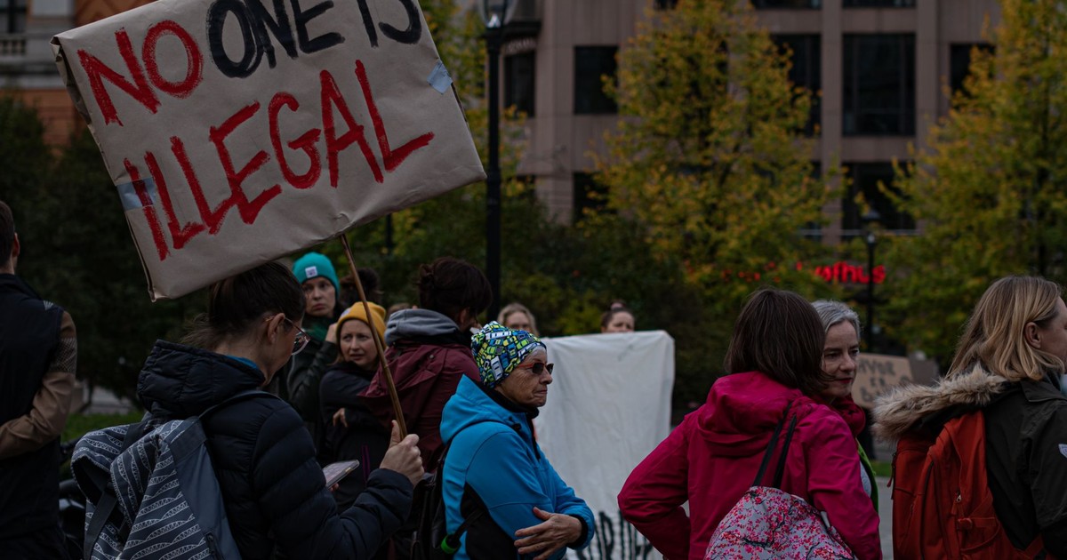 A group of diverse adults protesting immigration policies with signs outdoors.