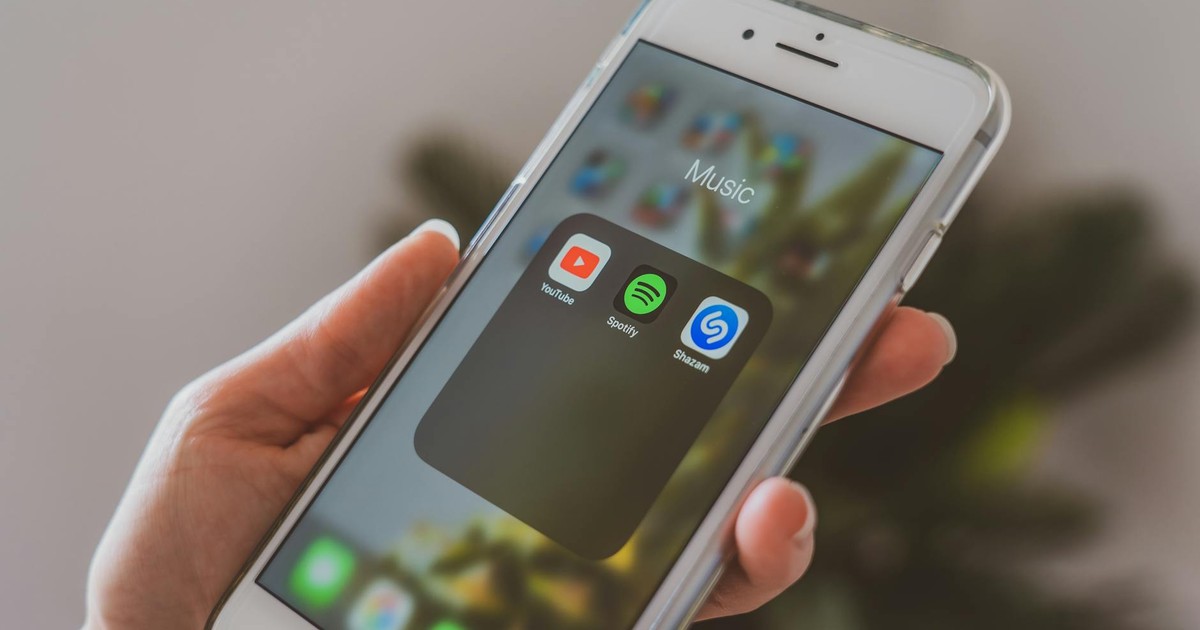 Hand holding a smartphone displaying popular music apps like Spotify and Shazam in a close-up shot.