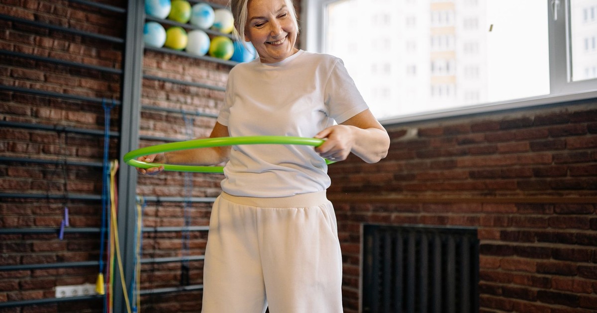 Smiling senior woman exercises with a hula hoop, promoting fitness and fun.