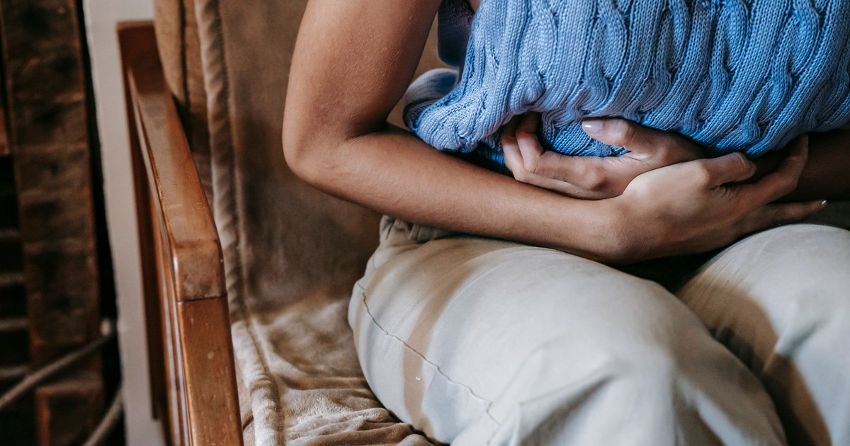 Crop unrecognizable female touching belly while having acute pain in stomach sitting on couch