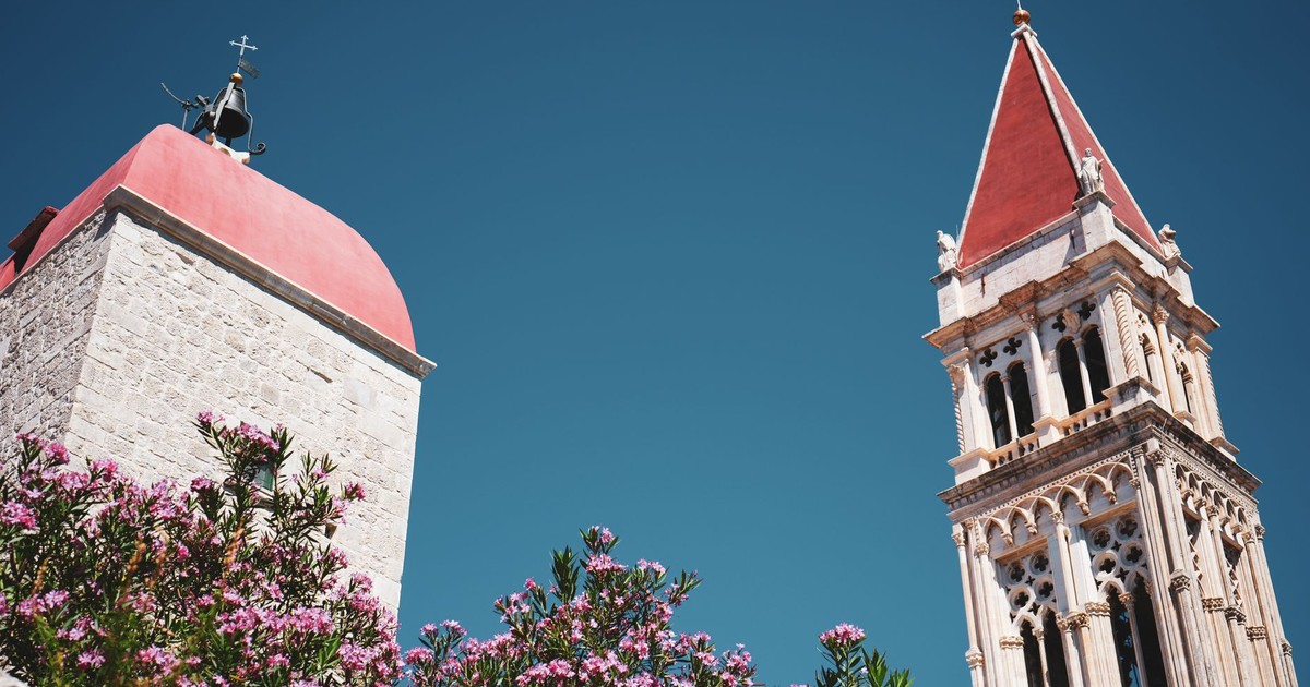 Historic bell towers with red roofs, surrounded by pink flowers under a clear blue sky.