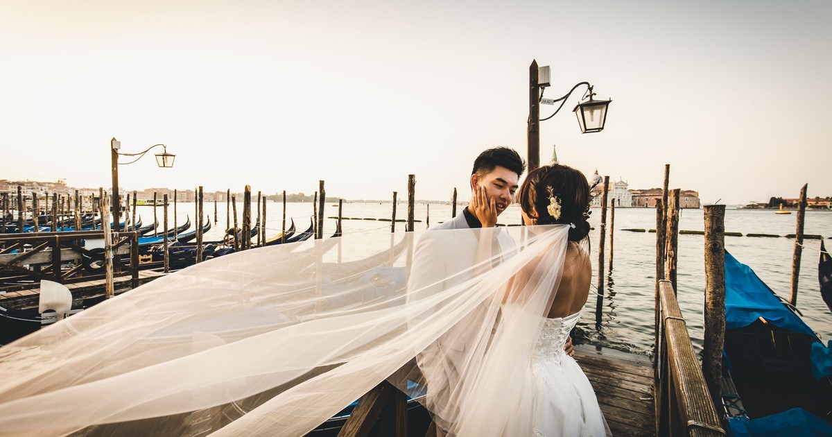 Couple embracing on a Venetian dock with flowing veil at sunset.