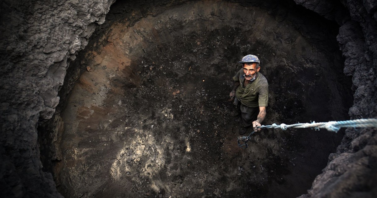 A man stands in a deep pit holding a rope, looking up from a high angle view.