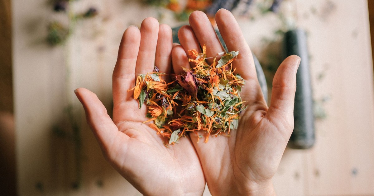 Close-up of hands holding a mix of vibrant dried herbs on a wooden surface.