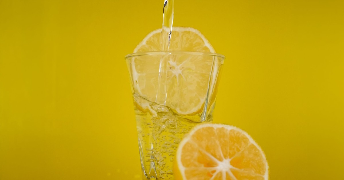 A close-up of water pouring into a glass with lemon slices, vibrant yellow backdrop.
