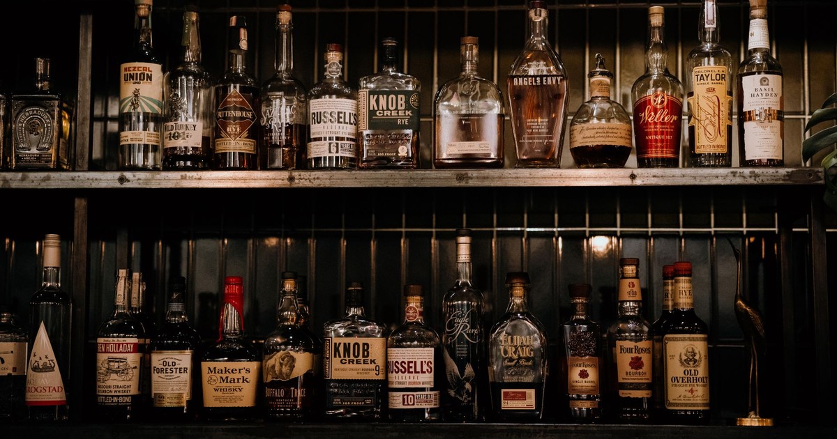 A variety of liquor bottles arranged on shelves in a dimly lit bar setting.