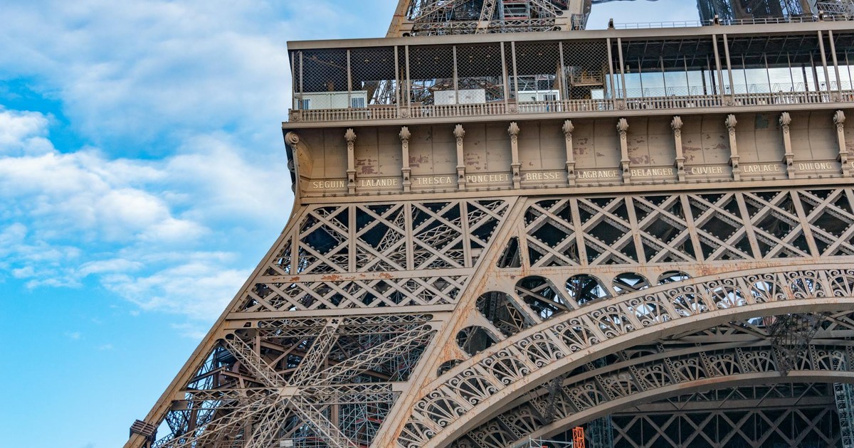 Detailed view of the Eiffel Tower's intricate ironwork against a vibrant blue sky.