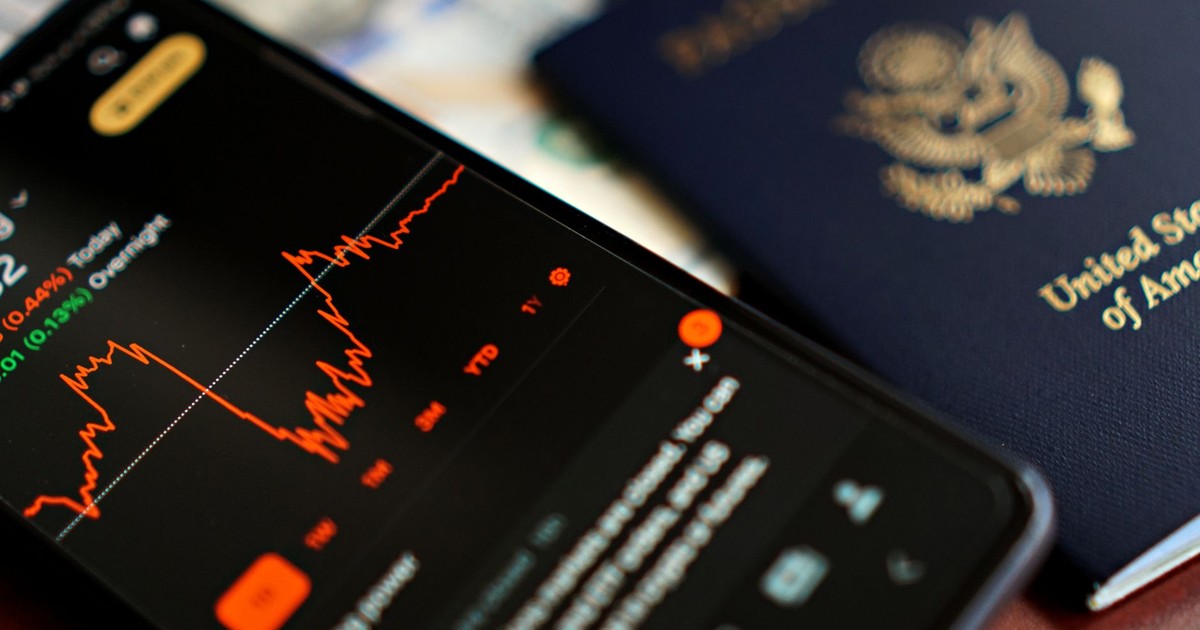 Close-up of a smartphone displaying stock data next to a US passport, suggesting travel and finance themes.