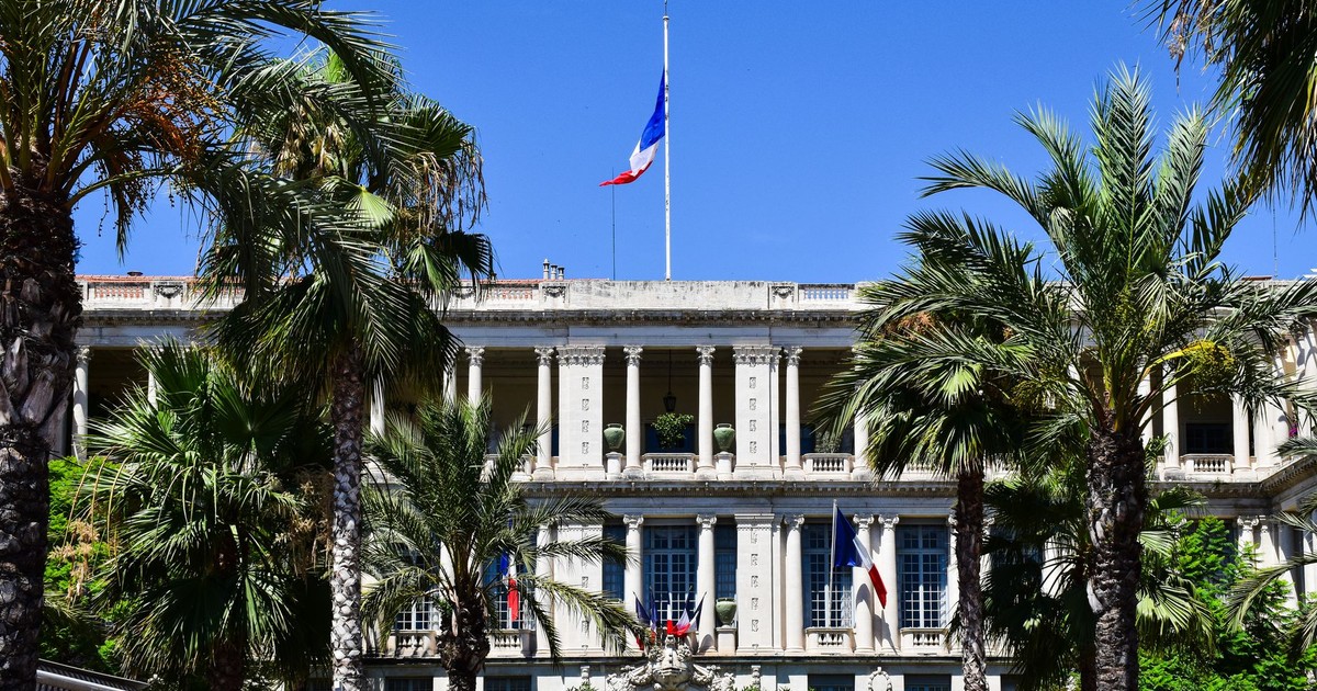 Elegant French colonial-style building surrounded by palm trees in Nice, France.