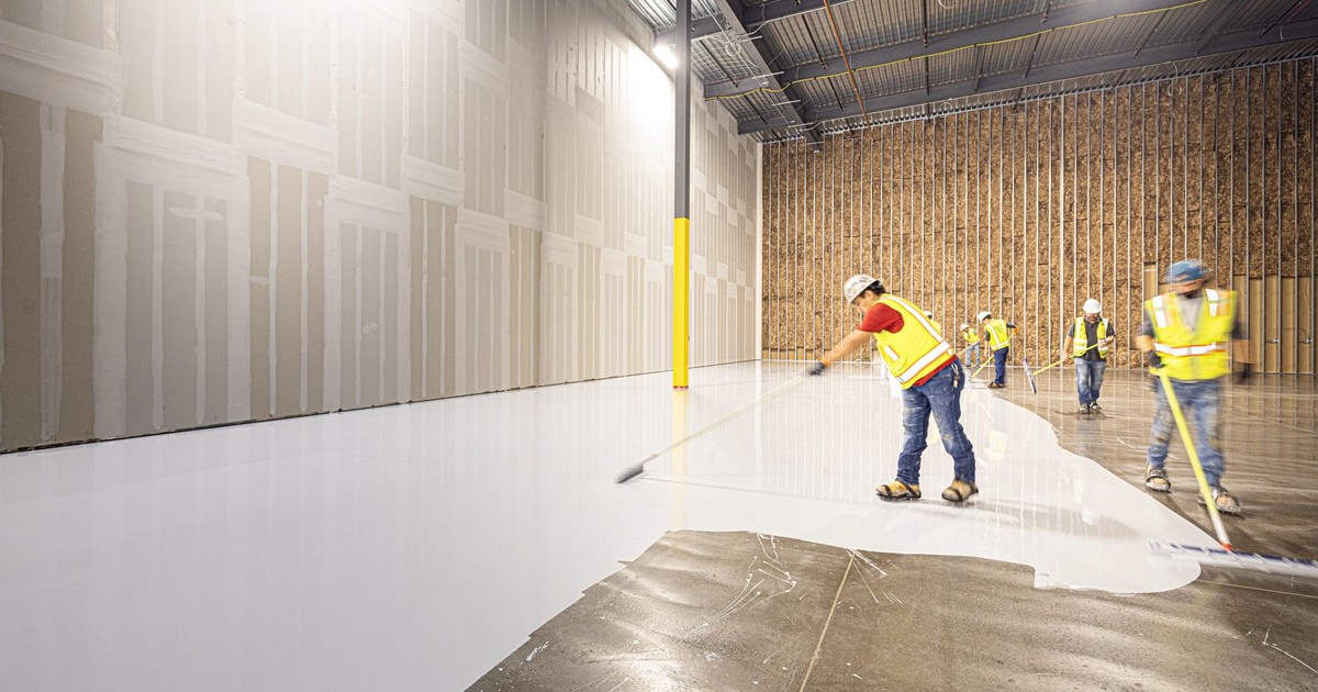 Construction workers in hard hats and vests laying a fresh concrete floor inside a building in Dallas, Texas.
