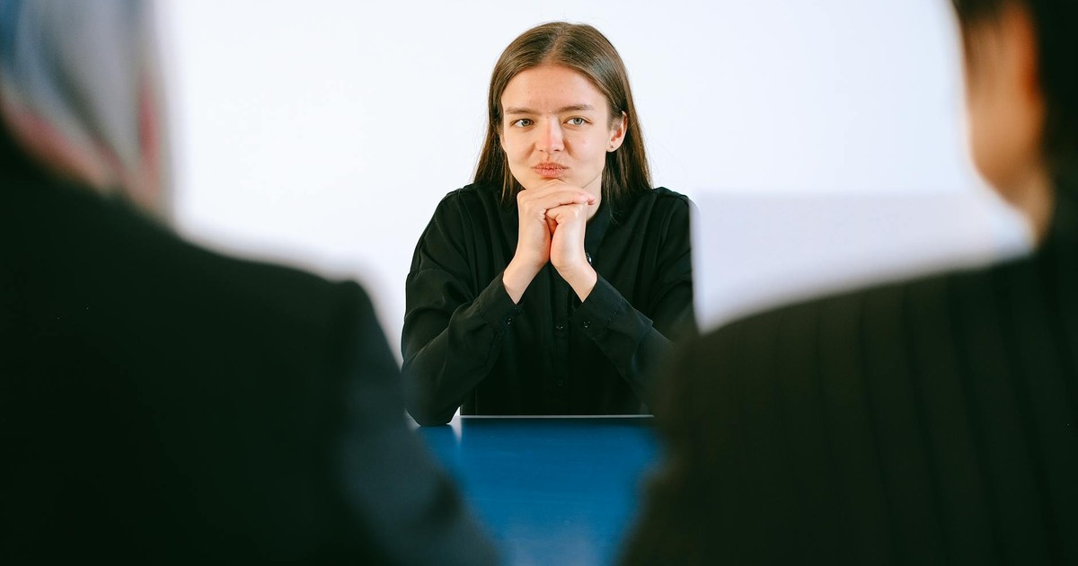 A woman in a job interview facing two people at an office table, focusing intently.