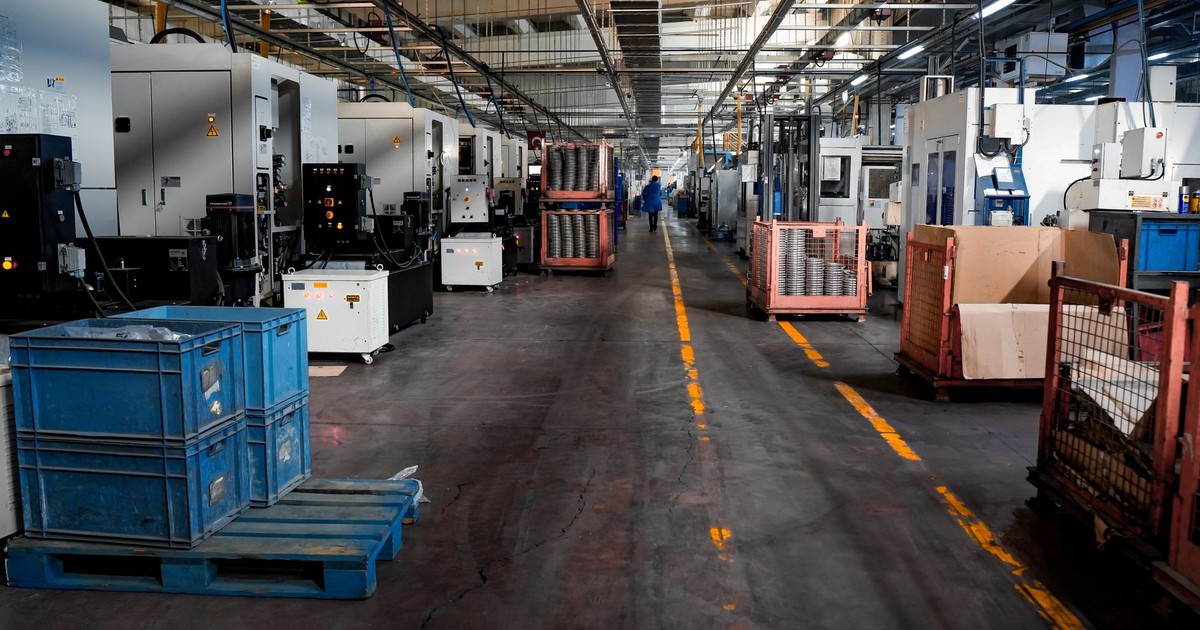 Vast industrial factory floor with machinery, crates, and structured workstations.