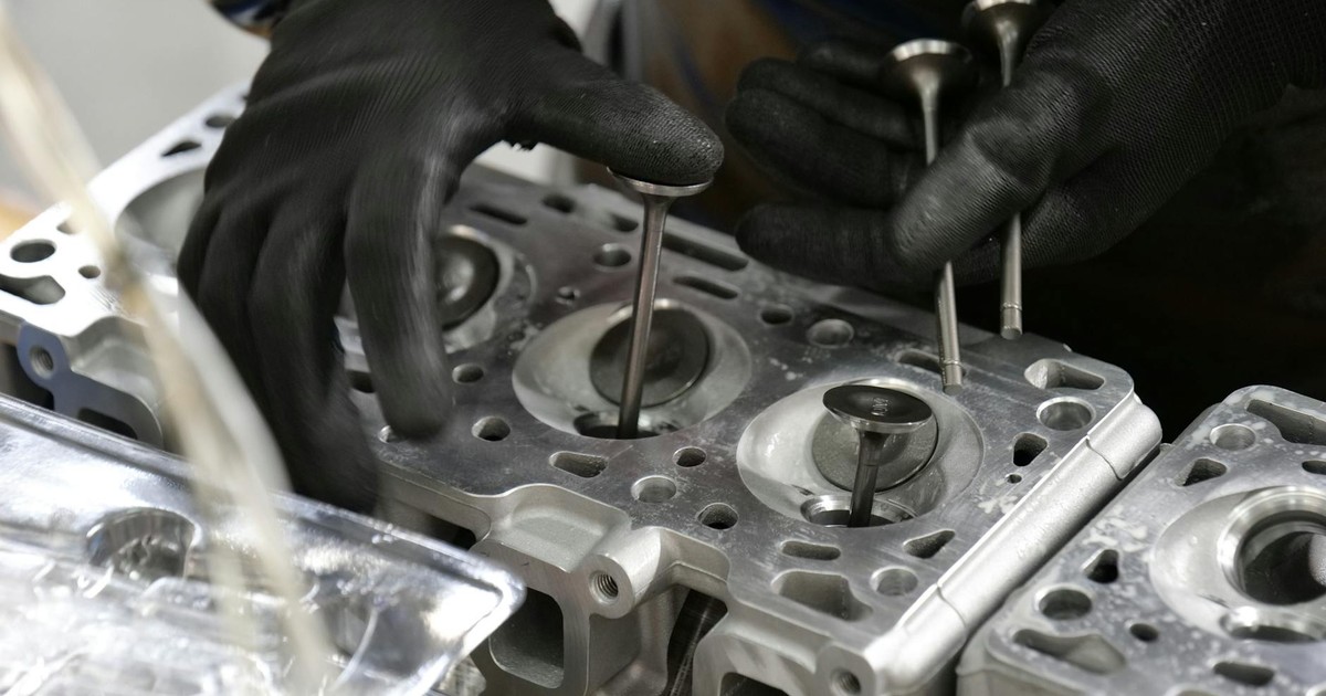 Close-up of mechanic's hands working on engine cylinder head assembly with valves.