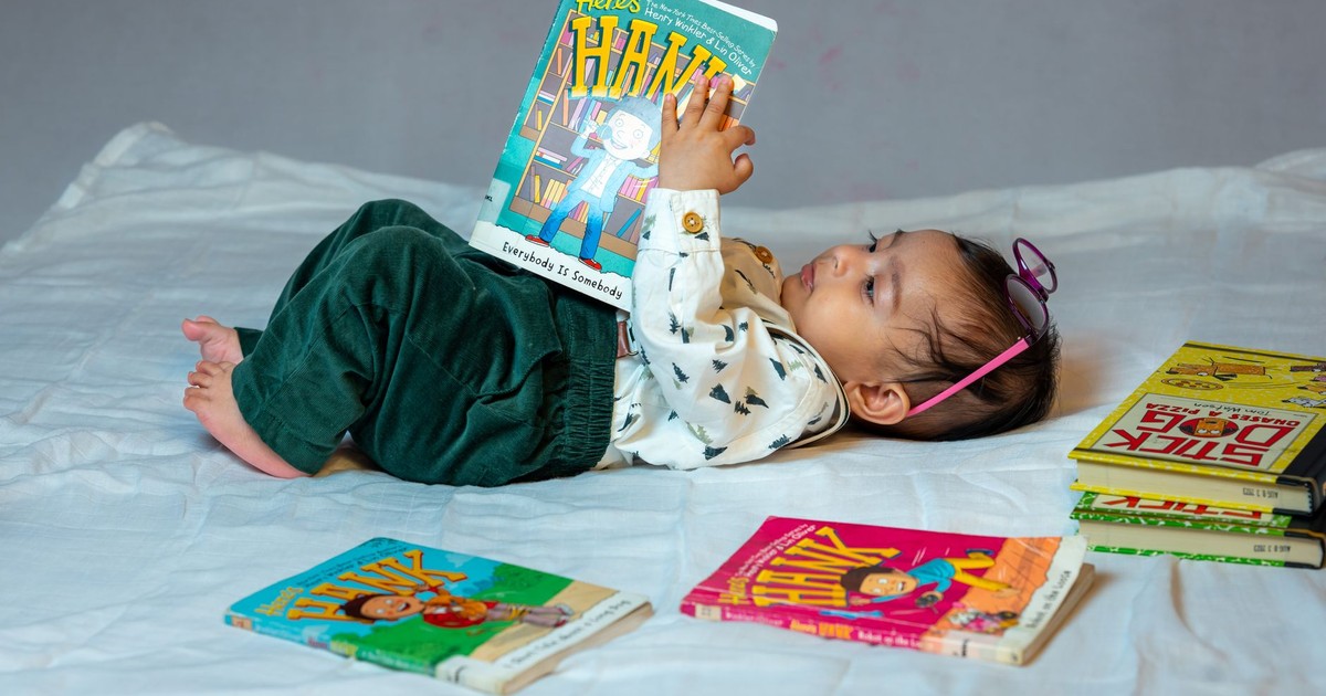 A cute baby lying on a bed, reading colorful children's books with enthusiasm. Captivating scene of early childhood learning.