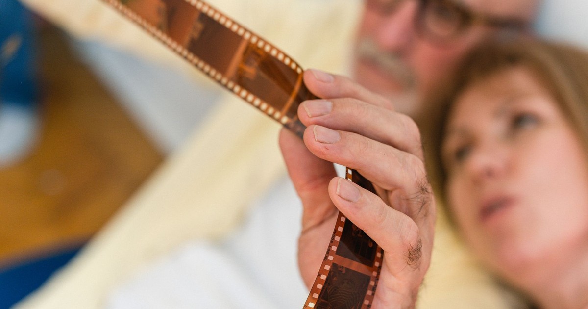 An elderly couple intently examining an old photographic film strip together indoors.