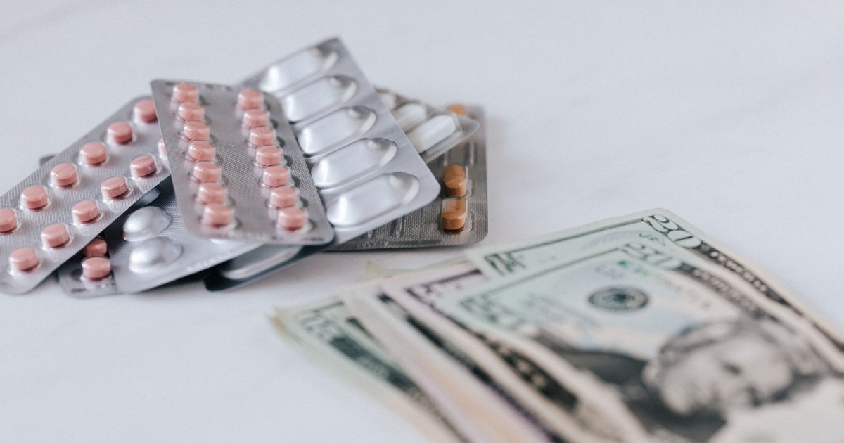Multicolored pills in silver blisters on white surface near heap of paper money representing expensive pharmacy