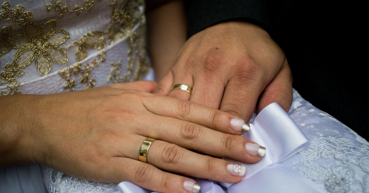 Detailed shot of newlyweds' hands with wedding rings, adorned with intricate lace and embroideries.