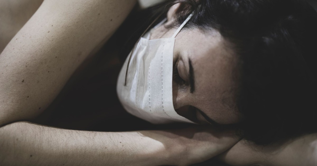 Freckled woman with mask sleeping indoors, representing fatigue and recovery.