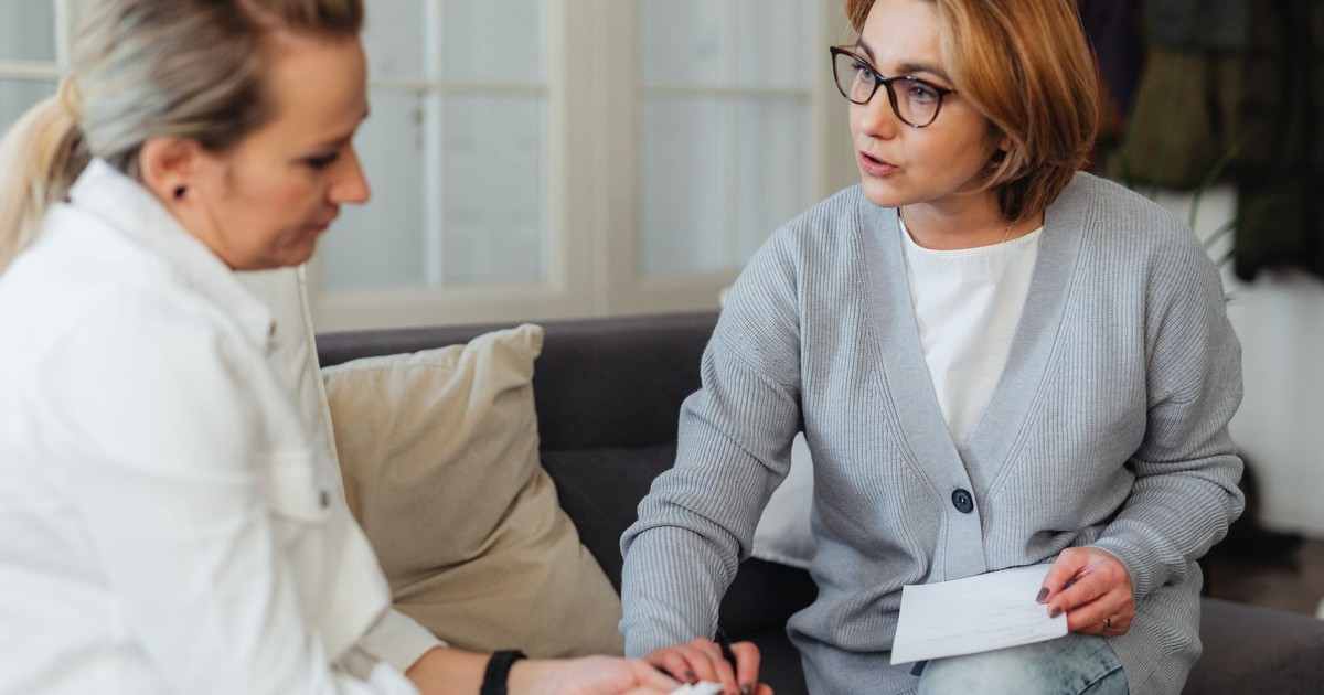 Two adult women sitting indoors having a thoughtful conversation on a couch.