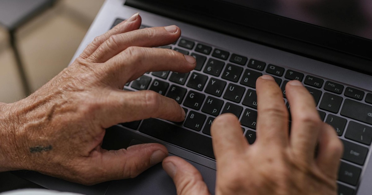 Close-up of senior adult hands typing on a laptop keyboard, viewed from above.