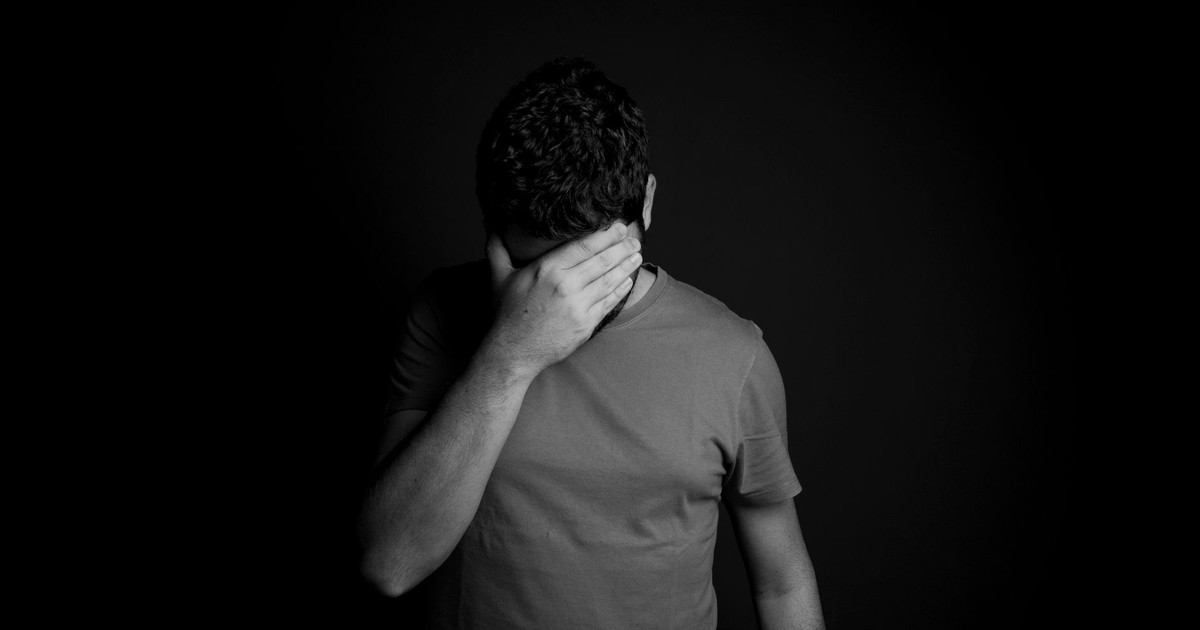 A black and white portrait of a man hiding his face, conveying deep emotion and introspection.
