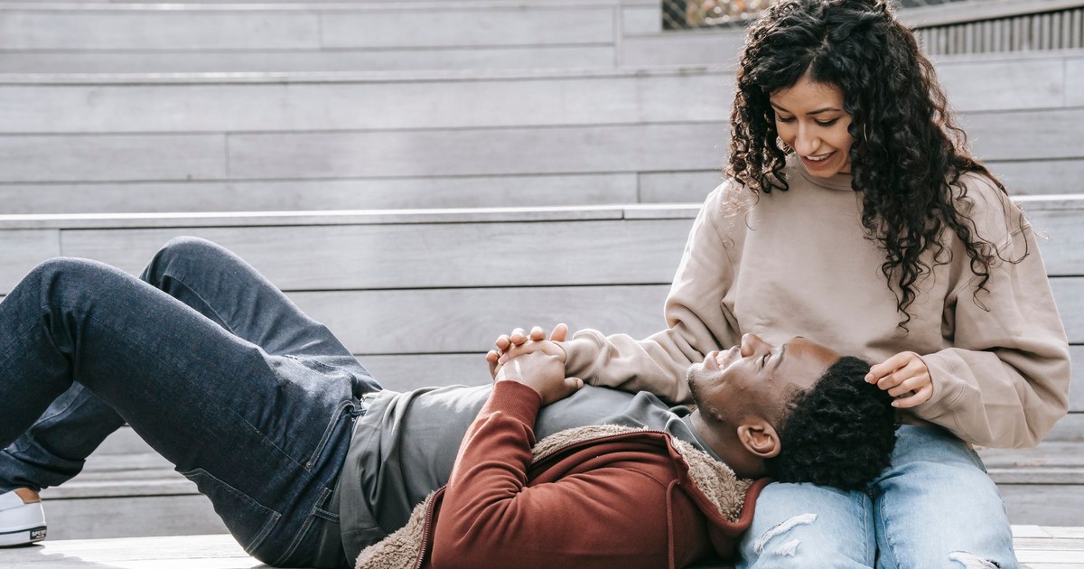 Cheerful African American boyfriend lying on lap of ethnic girlfriend and looking at each other while sitting on wooden stairs on street during date