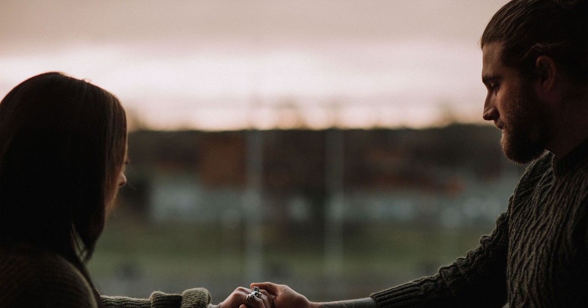 Side view of crop unshaven male holding hand of female beloved on balcony at sundown