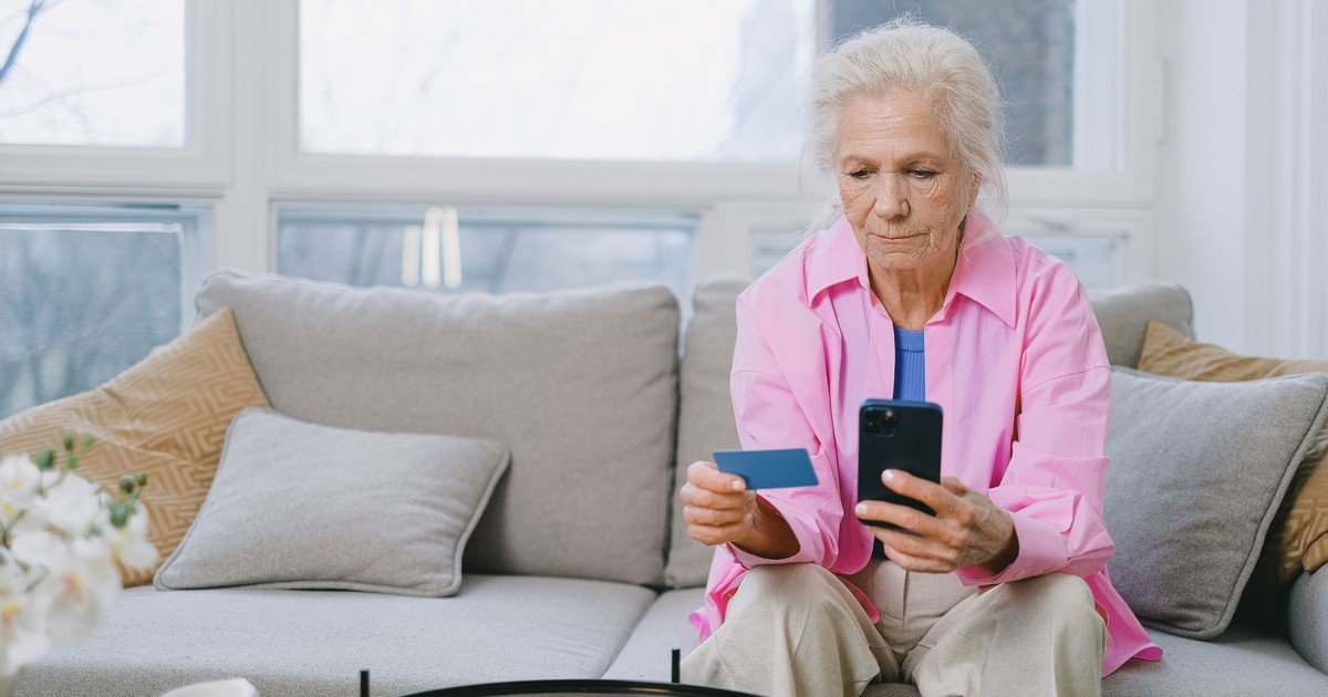 Elderly woman shopping online using smartphone and credit card indoors.
