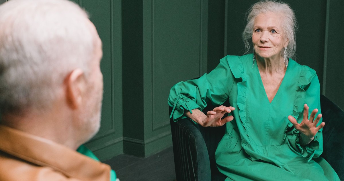 Senior couple seated indoors having an engaging conversation. Warm expressions and gestures highlight their emotions.