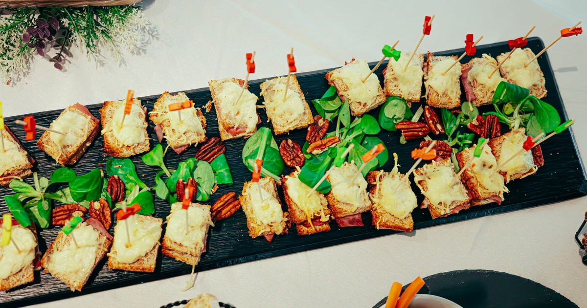 Gourmet appetizers on black platter garnished with pecans and greens.